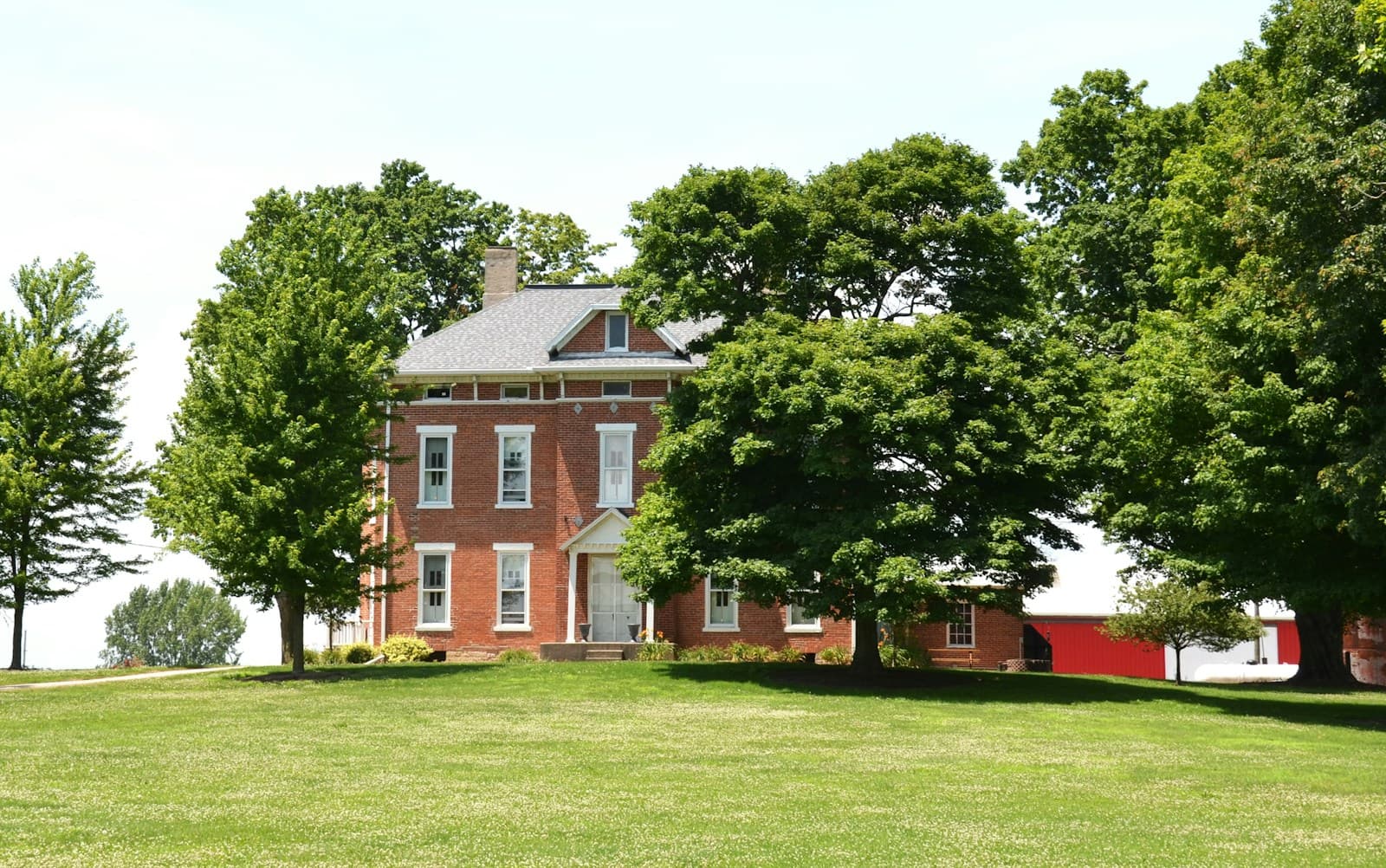 A broad green lawn under mature trees in front of a brick home.