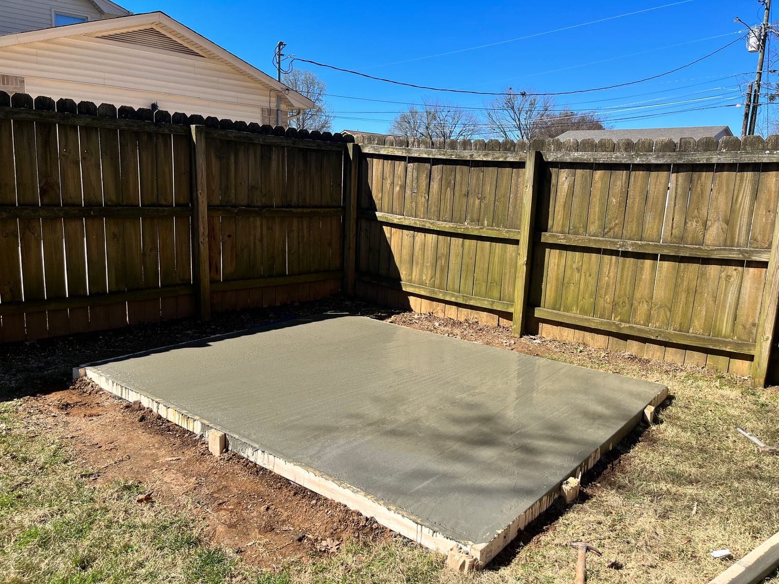 A finished concrete pad poured and floated smooth inside its forms in a fenced back yard.
