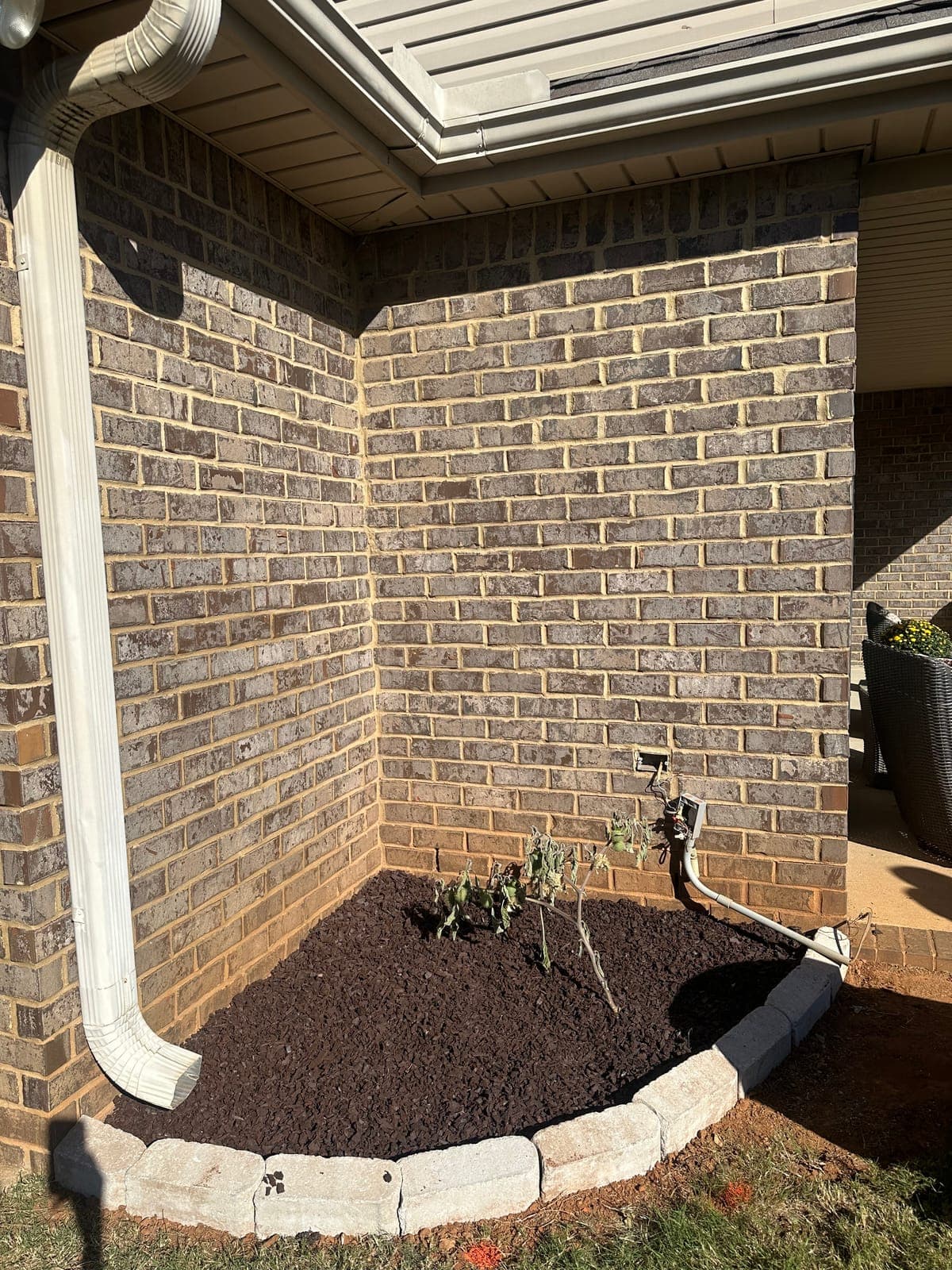 Fresh black mulch spread level in a stone edged bed tucked into the corner of a brick house.