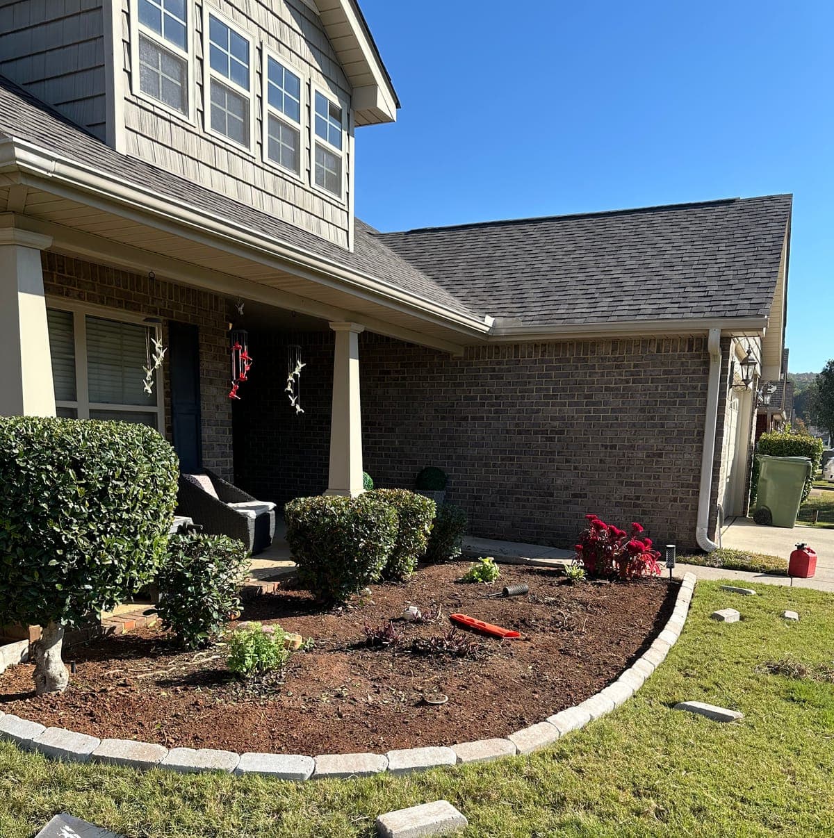 A deep front bed edged in tan pavers, freshly turned and planted with clipped shrubs against a brick home.